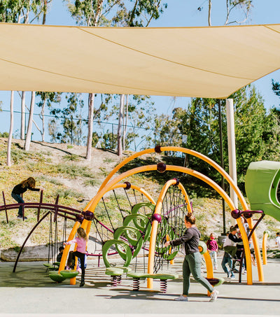 Children playing on a colorful playground structure with a canopy in an outdoor setting.