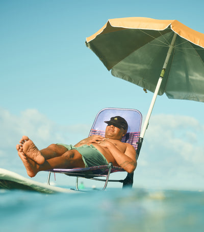 Man relaxing on a beach chair under an umbrella with clear blue sky and ocean.