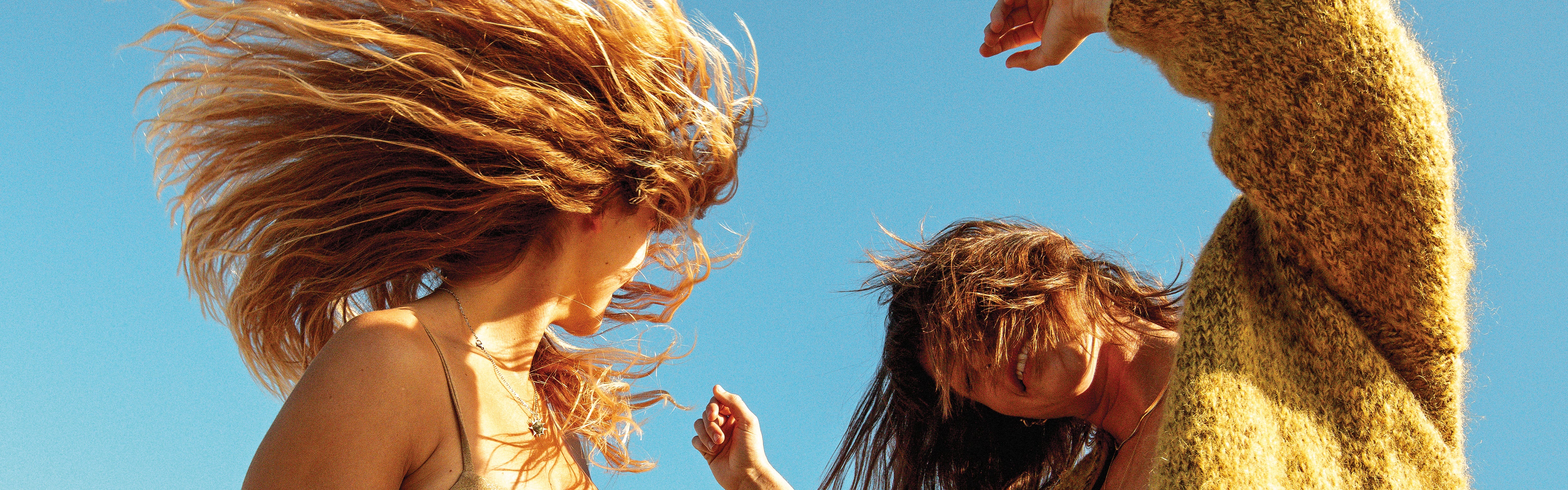 Woman flipping sun-kissed hair under blue sky, showcasing beachy texture and shine – Hair Collection - Sun Bum.
