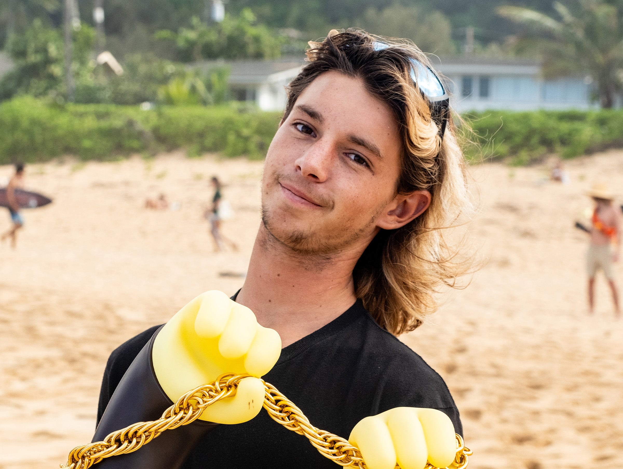 Man on a beach wearing a black shirt with yellow dumbbells and a gold chain