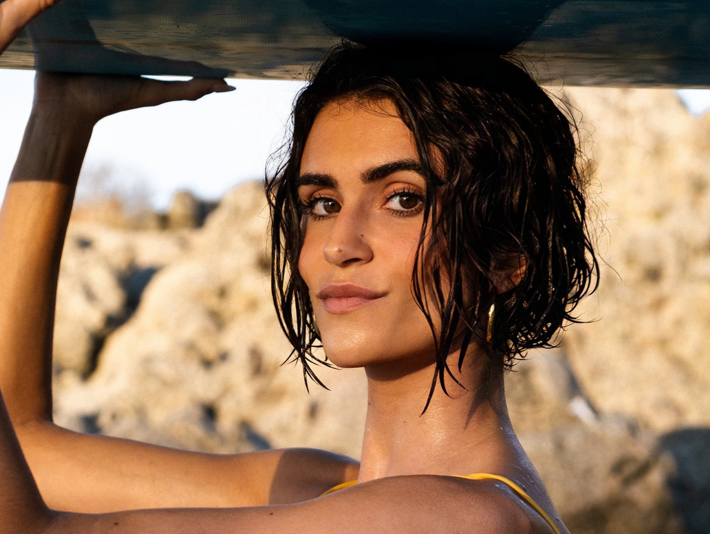 Woman holding a surfboard with a rocky landscape in the background
