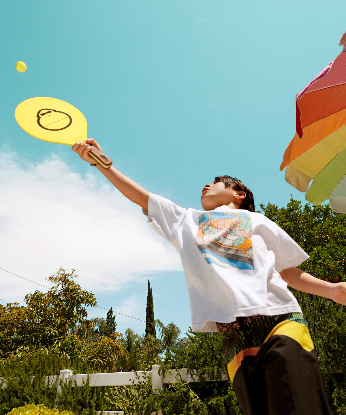 Person playing with a yellow disc in an outdoor setting with trees and a clear sky.