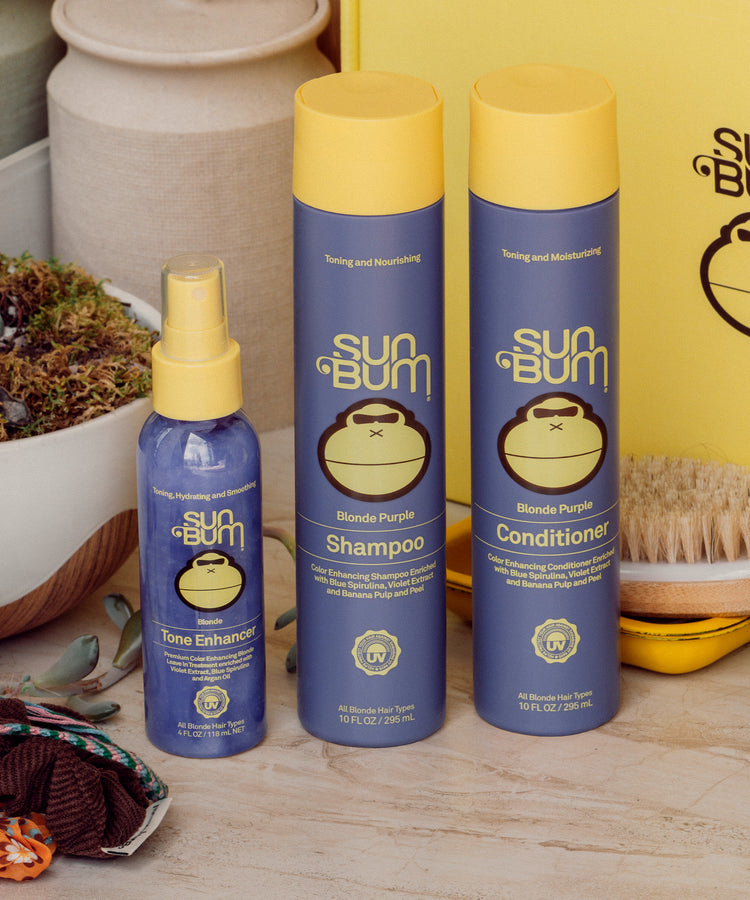 Sun Bum hair care products including shampoo, conditioner, and tone enhancer on a wooden surface.